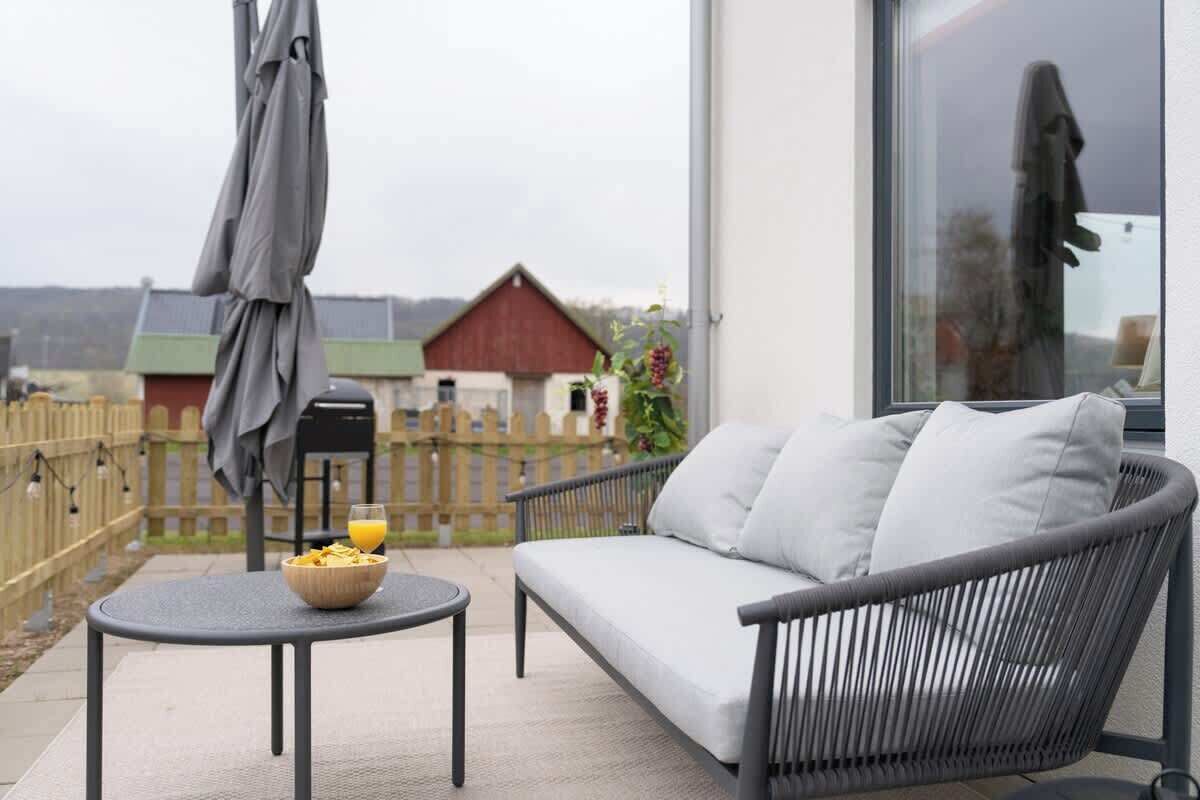 A balcony with a sofa, a small round table with a bowl of fruit and a glass of orange juice, and a large window.