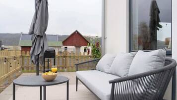 A balcony with a sofa, a small round table with a bowl of fruit and a glass of orange juice, and a large window.