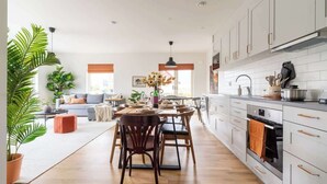 Una cocina moderna con armarios blancos, un comedor con mesa y sillas, y una sala de estar con sofá y una mesa de centro.