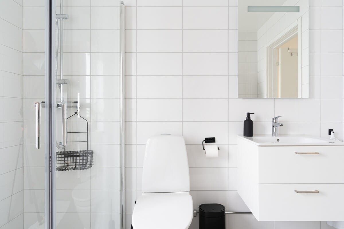 Ein modernes Badezimmer mit Duschkabine aus Glas, einer weißen Toilette und einem weißen Waschtisch mit Spiegel.
