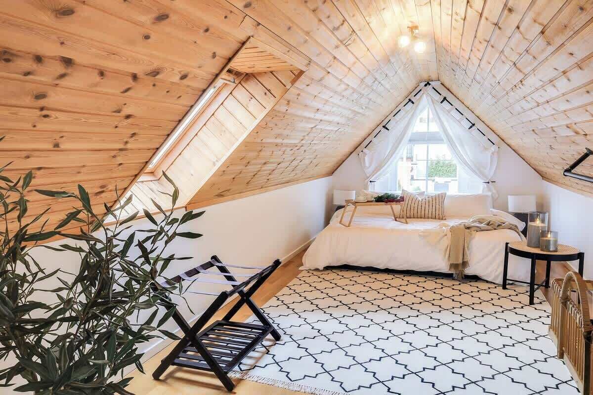 A cozy attic bedroom with a sloped ceiling, a bed, a bedside table, and a window.