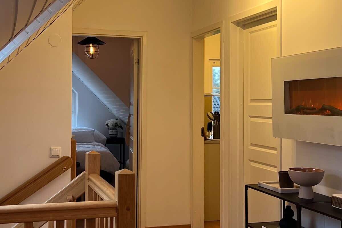 A hallway with a staircase leading to a bedroom, a small table with a bowl and a cup, and a wall-mounted television.