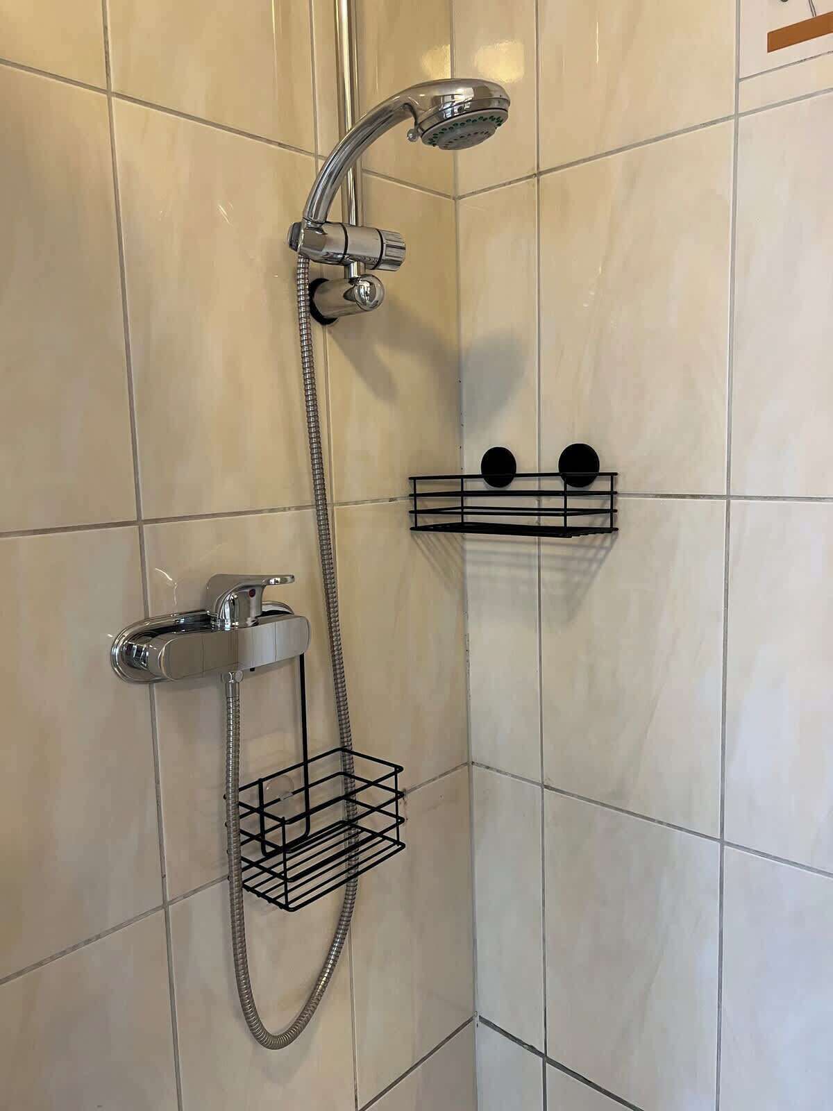 A shower with a handheld showerhead and a wall-mounted faucet, with two black towel racks on the wall.