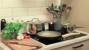 A kitchen with a wooden cutting board, a knife, a frying pan, a pot, and a stove. - Fully Equipped Home Close to Malmo Copenhagen (Vellinge)