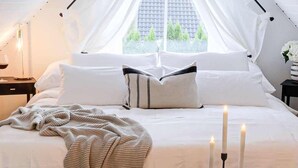 A neatly made bed with white linens, a knitted blanket, and three lit candles on a bedside table. - Fully Equipped Home Close to Malmo Copenhagen (Vellinge)