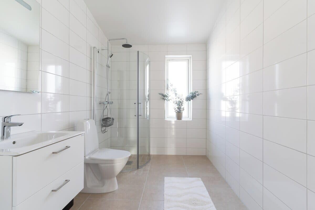 A modern bathroom with white tiles, a glass shower enclosure, a white sink, and a toilet.