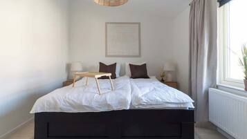 A bedroom with a large bed, bedside lamps, a small table, and a window with curtains.