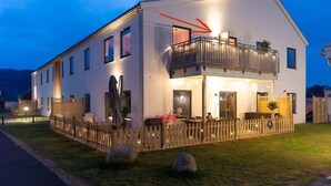 Un edificio de dos pisos con balcón, cerca de madera y una entrada bien iluminada.