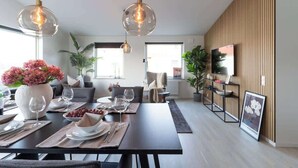 Un comedor moderno con una mesa de madera oscura, lámparas colgantes de vidrio transparente y un jarrón grande lleno de flores rosadas.