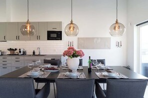 A modern kitchen with white cabinets, a central island with a vase of flowers, and pendant lighting. - Chocolaty Warmth Home 3BR Flat with Cozy Balcony (Båstad)