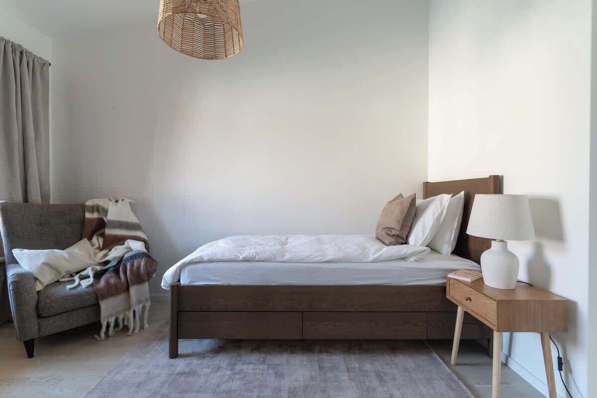 A bedroom with a bed, a nightstand, a lamp, a chair, and a hanging light fixture.