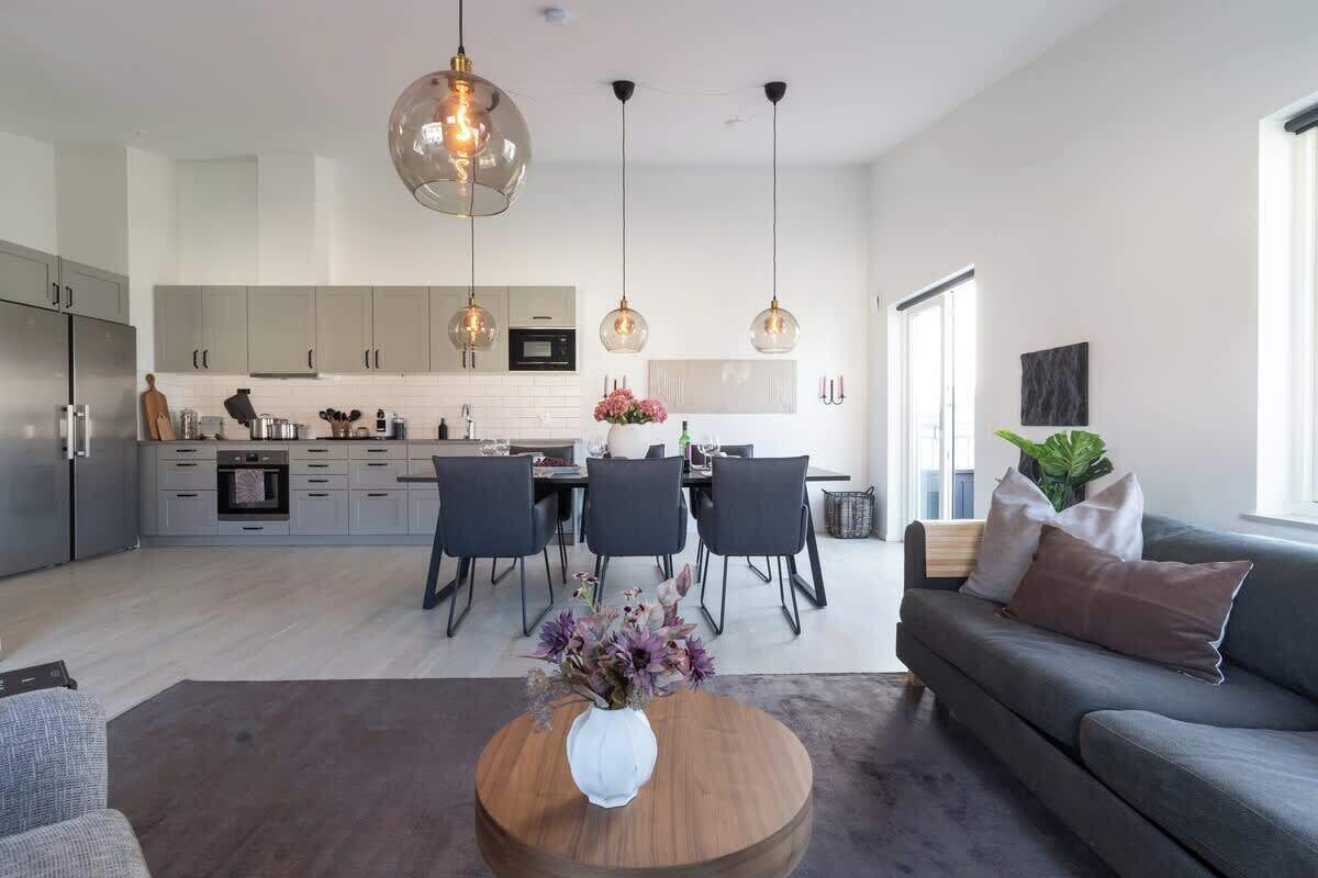 A modern kitchen with grey cabinets, a dining area with a table and chairs, and a grey sofa with cushions.