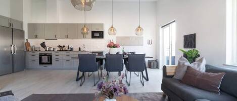 A modern kitchen with grey cabinets, a dining area with a table and chairs, and a grey sofa with cushions.