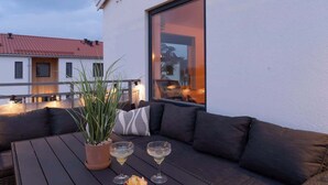 Un espacio de estar al aire libre con una mesa, dos bebidas, una planta en maceta y un sofá.