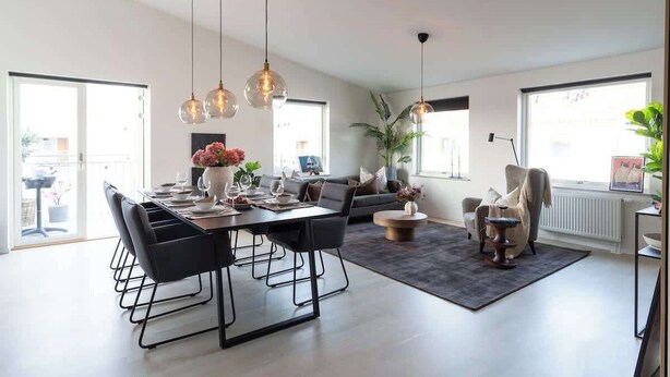 Una sala de estar moderna con comedor, ventanas grandes y un sofá gris.