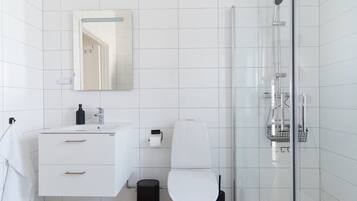 A modern bathroom with white tiles, a white sink, a toilet, a mirror, and a glass-enclosed shower area.