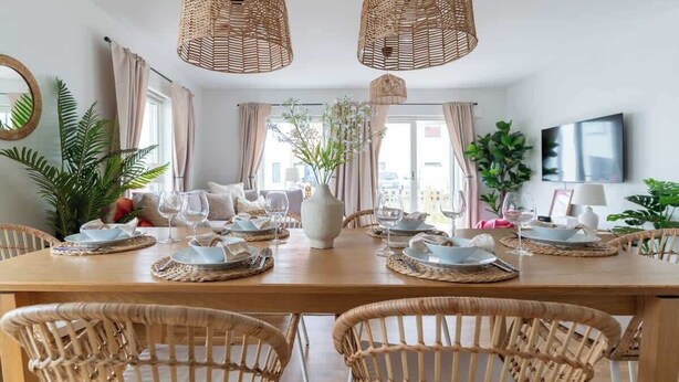 Un comedor con una mesa de madera dispuesta para cuatro personas, rodeado de sillas de mimbre.