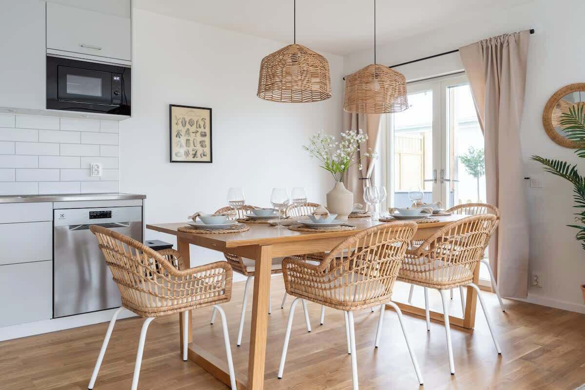Eine moderne Küche mit weißen Schränken, einer eingebauten Mikrowelle und einem Essbereich mit einem Holztisch und Korbstühlen.