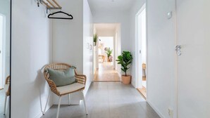 Un pasillo con una silla de mimbre, una planta en maceta y un perchero.