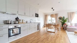Una cocina moderna con armarios blancos, electrodomésticos de acero inoxidable y un comedor con mesa y sillas de madera.