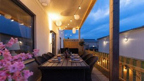 Un área de comedor al aire libre con una mesa larga, sillas de mimbre y luces colgantes.