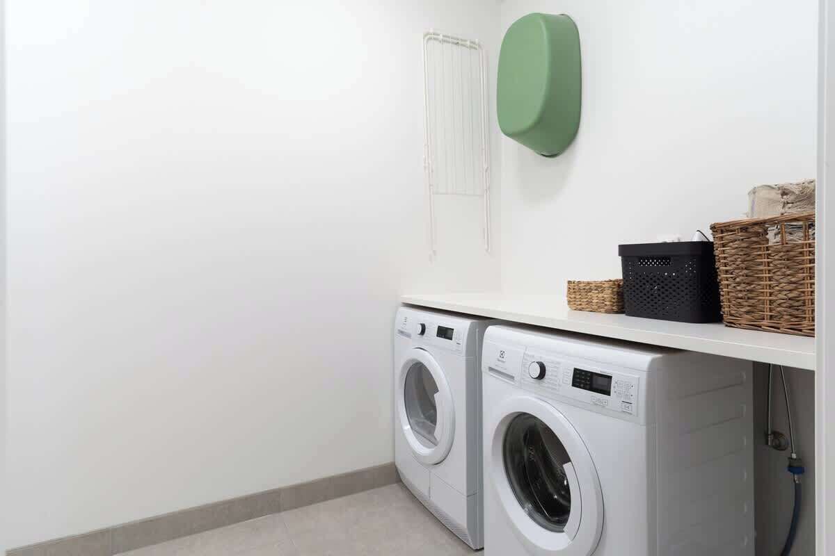 A laundry area with two front-loading washing machines, a drying rack, and baskets on a shelf.