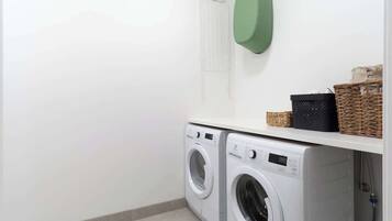 A laundry area with two front-loading washing machines, a drying rack, and baskets on a shelf.
