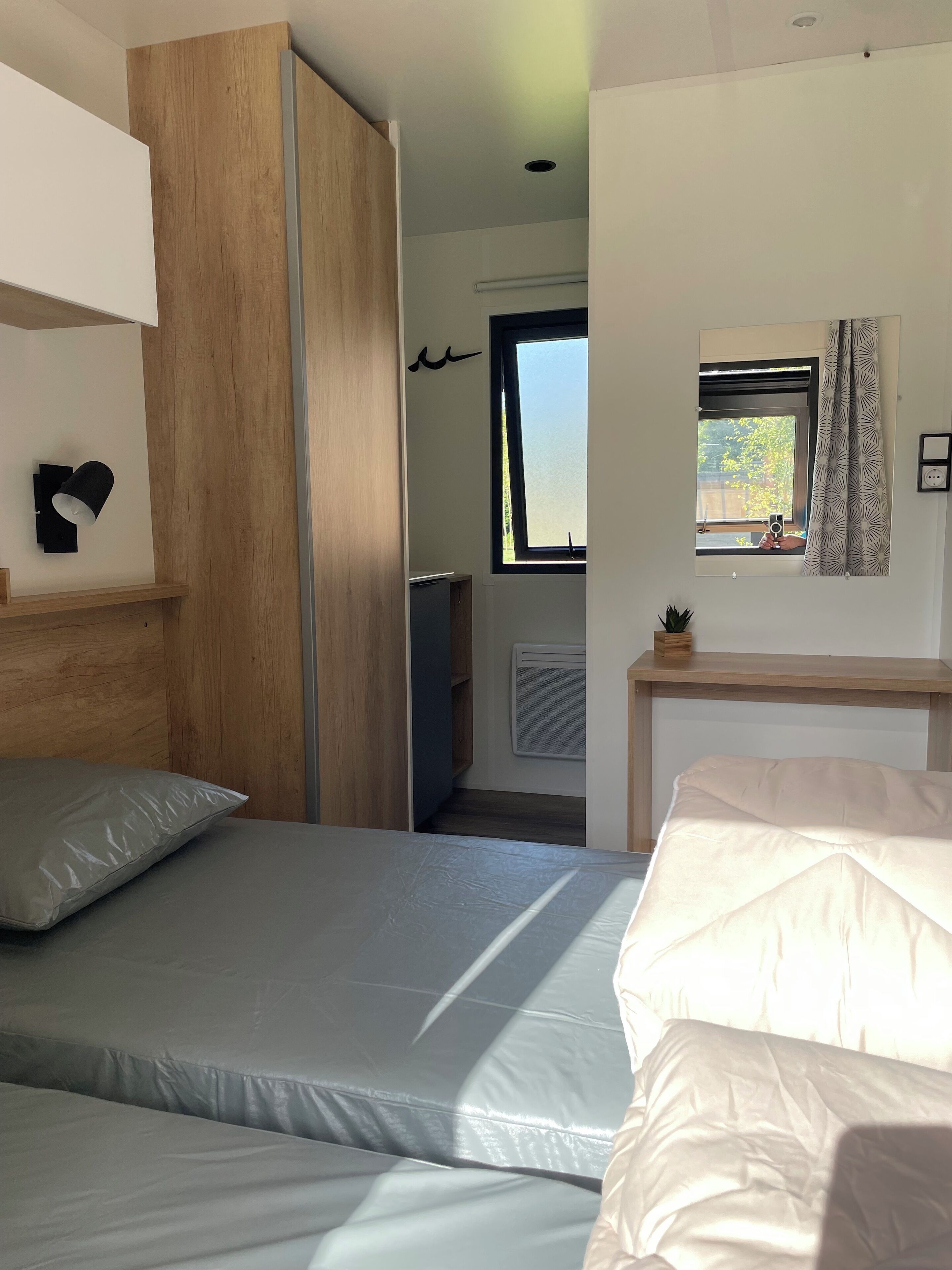 Un dormitorio con dos camas, un armario de madera, una mesita con una planta y una ventana con vistas al verdor.