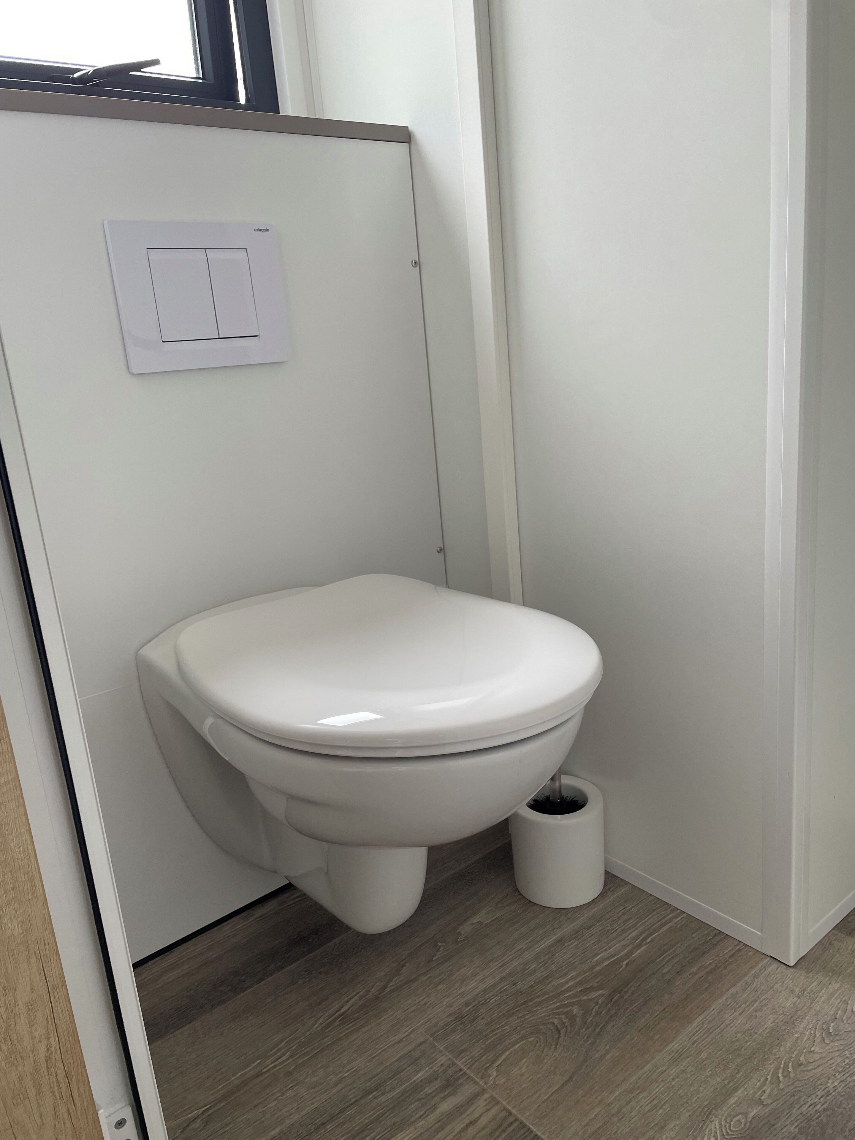 A small, modern bathroom with a white toilet, a wall-mounted flush handle, and a floor-mounted bidet.