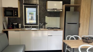 Een compacte kitchenette met een magnetron, koffiezetapparaat en gasfornuis. Er staat een eettafel met stoelen bij een raam.