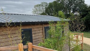 Een houten blokhut met een metalen dak, omgeven door een houten terras en weelderige begroeiing.