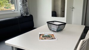 Een witte tafel met een tijdschrift, een zwarte mand en een zwarte bank in een kamer met een raam en een spiegel.