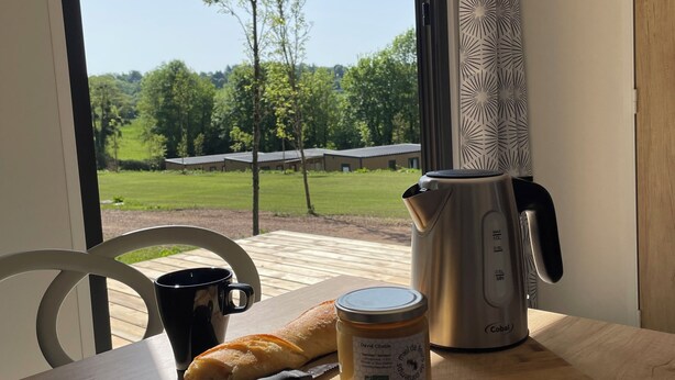 Een tafel met een brood, een pot jam, een koffiezetapparaat en een zwarte mok.
