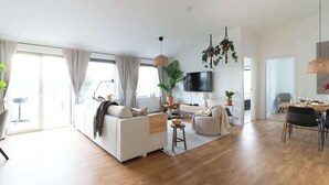 A spacious living area with a sofa, dining table, and chairs, a flat-screen TV mounted on the wall, and several potted plants. - Spacious Home with Workspace and Cozy Balcony (Båstad)