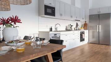 Una cocina moderna con armarios blancos, un refrigerador de acero inoxidable y un comedor de madera con sillas.