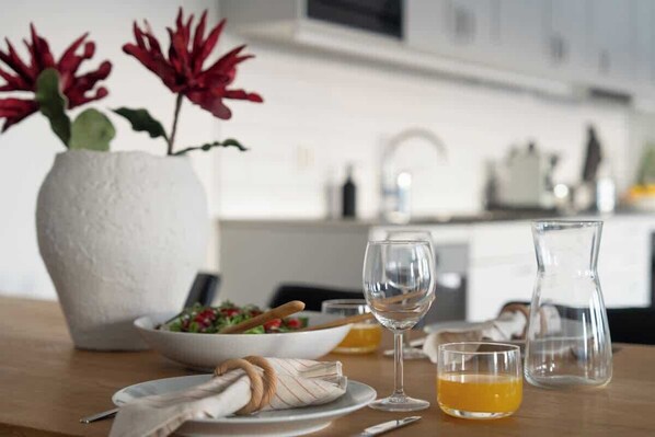 Une table à manger avec un vase blanc, un saladier, un verre à vin et une carafe.