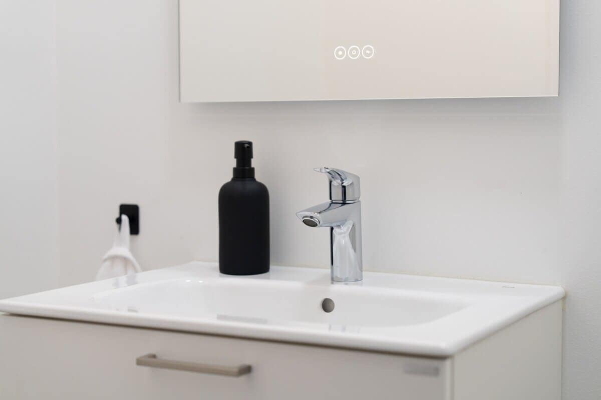 Un bany modern amb un lavabo blanc, una ampolla negra i un aixeta cromada.