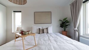 A bedroom with a large bed, a bedside table with a bowl and a cup, a potted plant, and a window with curtains. - Spacious Home with Workspace and Cozy Balcony (Båstad)