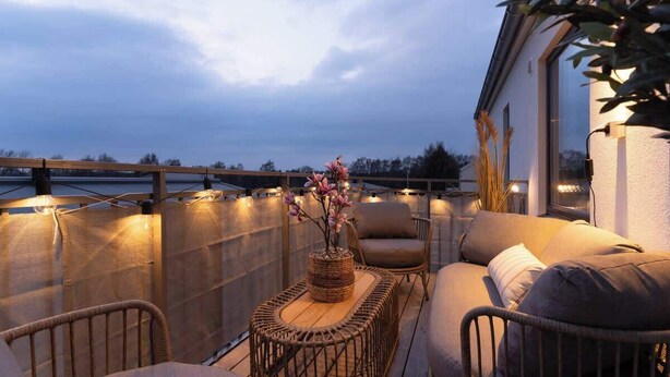 A balcony with a wicker table, cushioned seating, and a vase of flowers. - Spacious Home with Workspace and Cozy Balcony (Båstad)