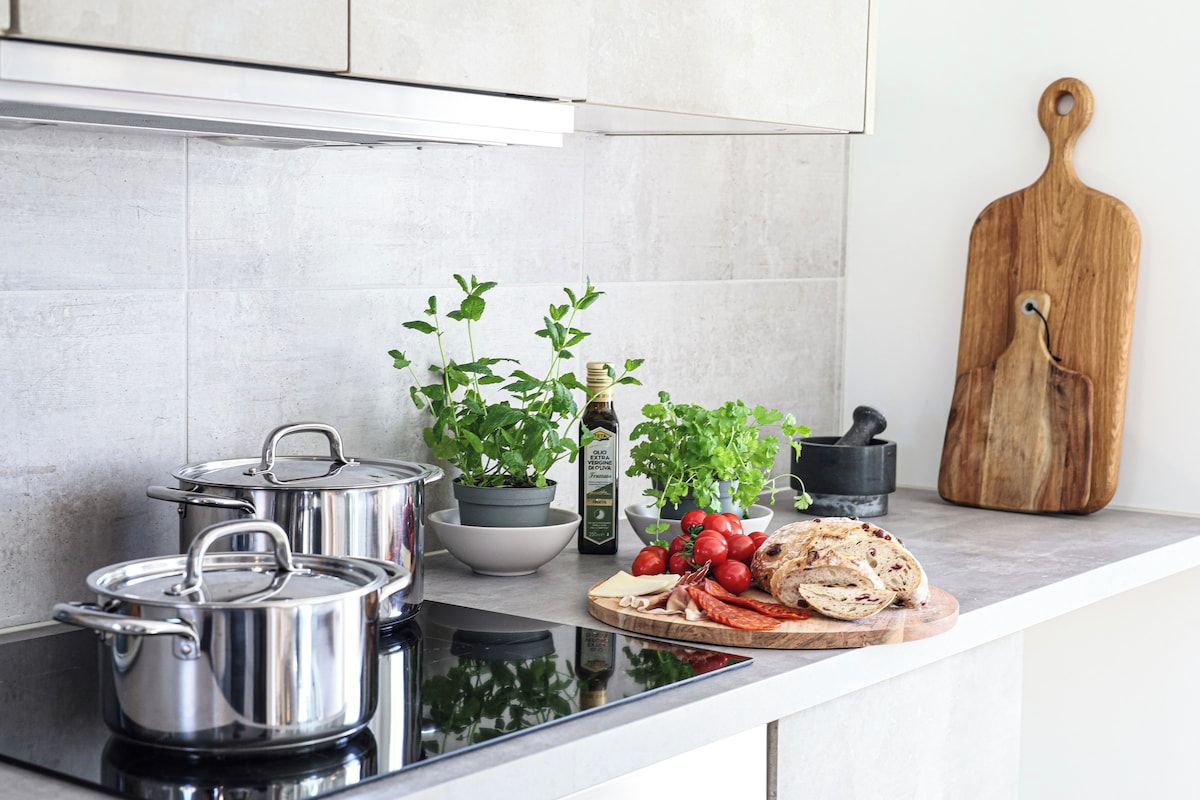 Una cocina con ollas de acero inoxidable, una tabla de cortar con verduras y una tabla de madera.