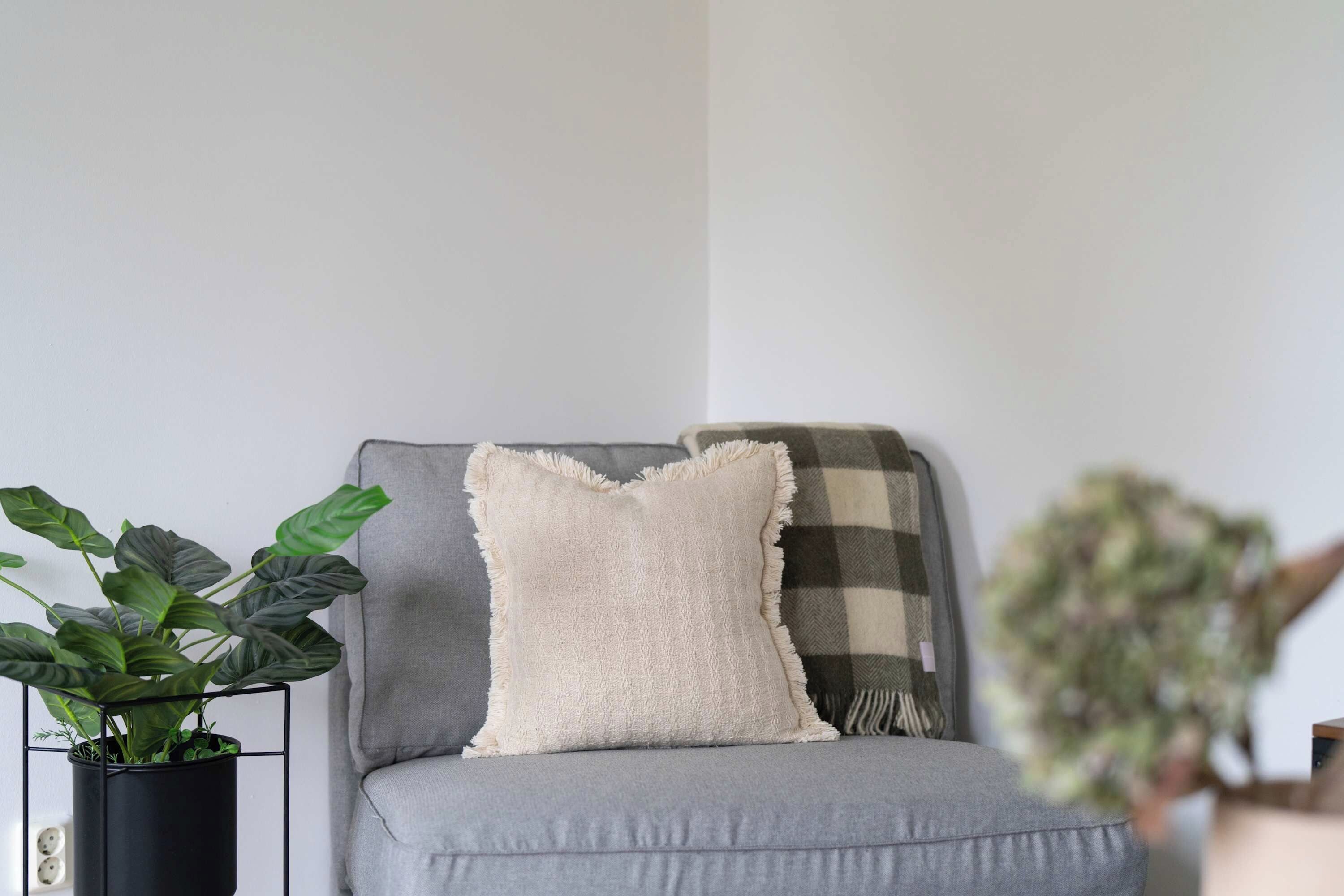 A grey sofa with a white cushion and a plaid blanket.