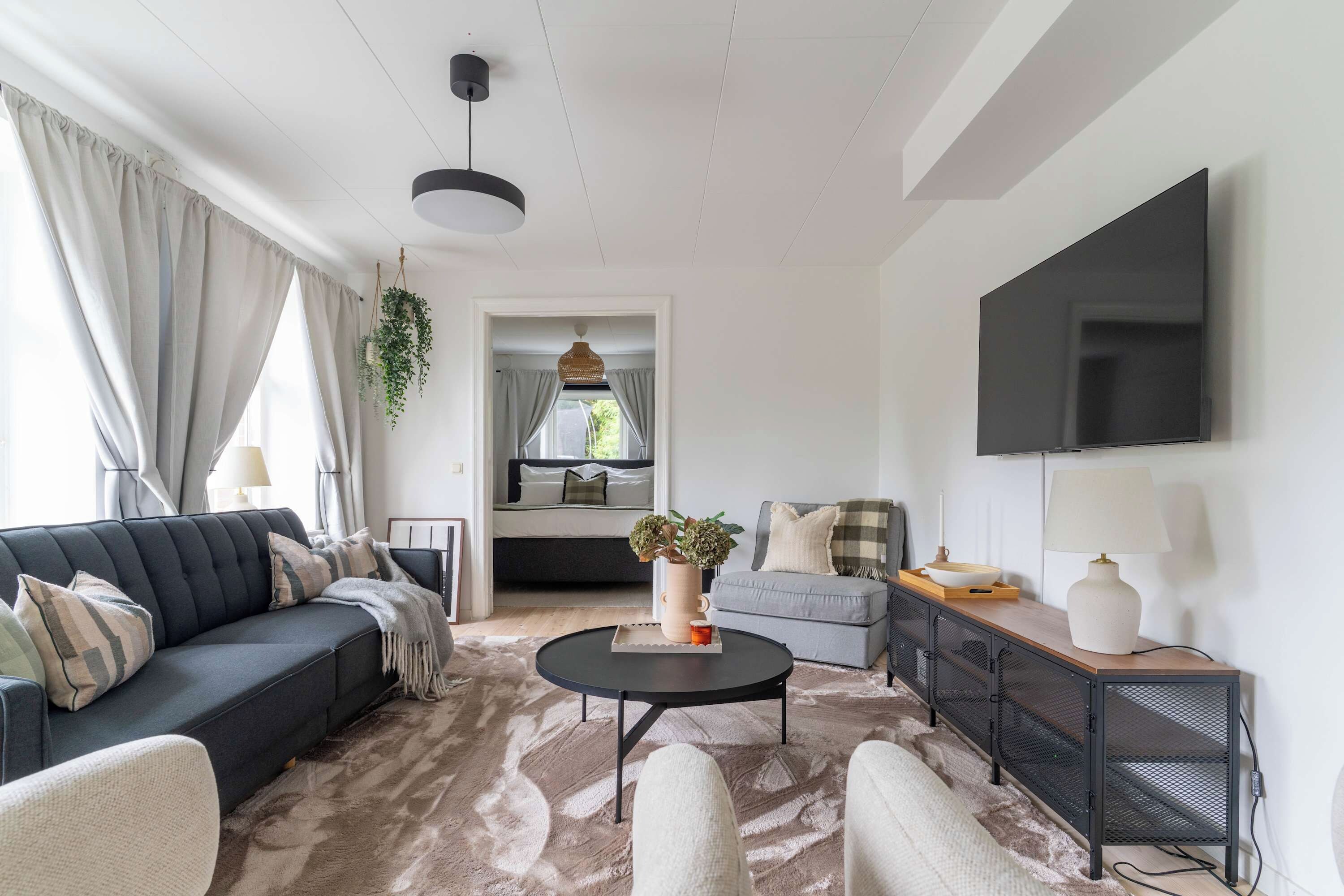 Ein modernes Wohnzimmer mit einer Couch, Sesseln, einem Couchtisch und einem an der Wand befestigten Fernseher.