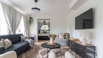 Ein modernes Wohnzimmer mit einer Couch, Sesseln, einem Couchtisch und einem an der Wand befestigten Fernseher.