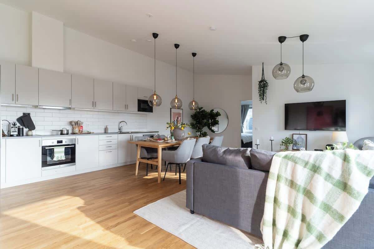 A modern kitchen with white cabinets, a dining area with a table and chairs, and a living room with a sofa and a TV.
