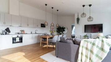 A modern kitchen with white cabinets, a dining area with a table and chairs, and a living room with a sofa and a TV.