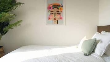 A bedroom with a bed, pillows, a framed artwork, and a potted plant.