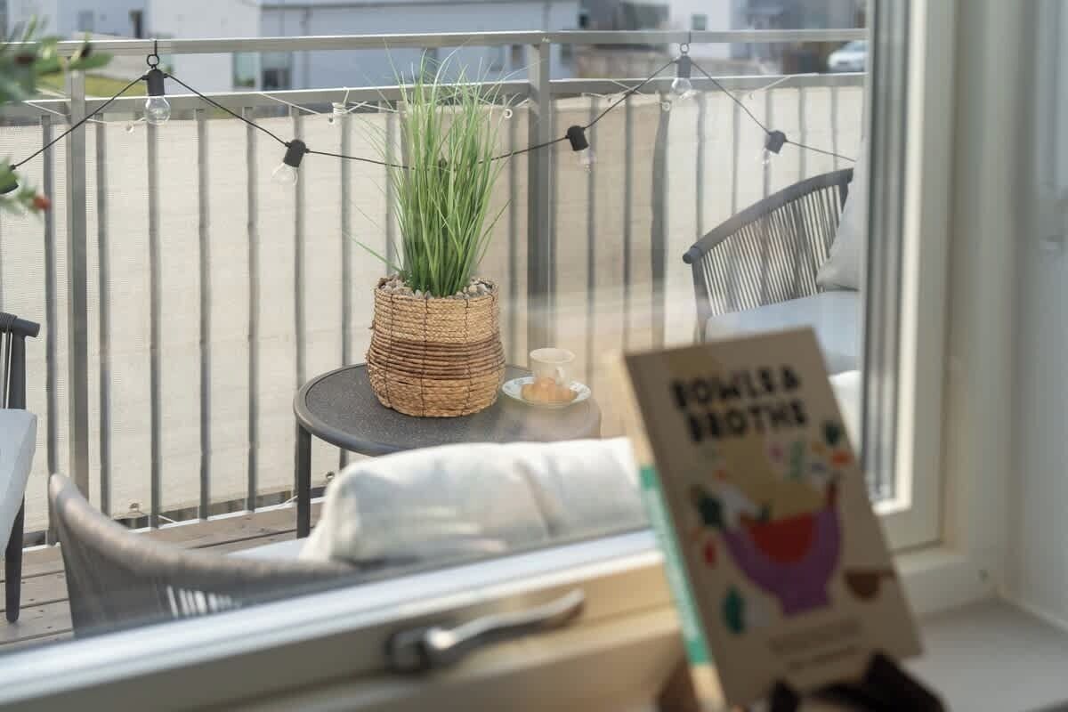 A balcony with a wicker plant pot, a small table with a candle, and a chair.
