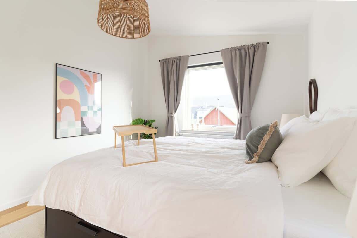 Une chambre avec un grand lit, une petite table, une lampe suspendue et une fenêtre avec des rideaux.