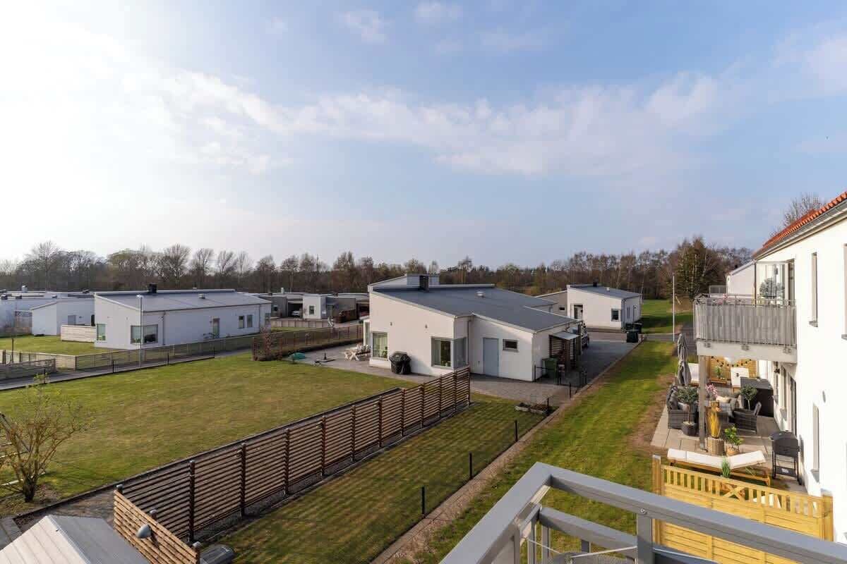 A residential area with modern houses, a grassy lawn, and a wooden fence.