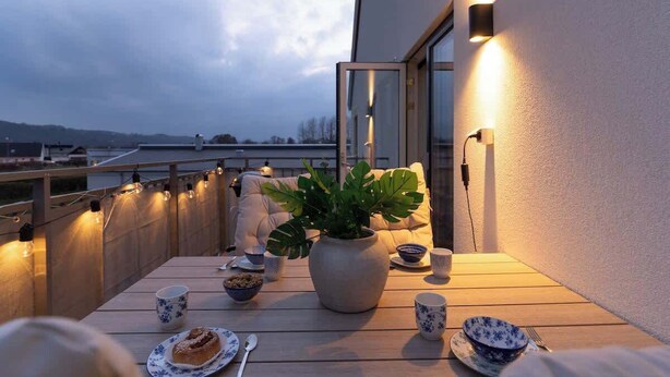 A balcony with a table set for tea, a potted plant, and a view of the cityscape.